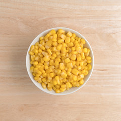 Organic sweet corn in a small bowl atop a wood table top view.