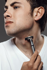 Young handsome man shaving over grey background.