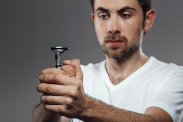 Young handsome man looking at shaver over grey background.