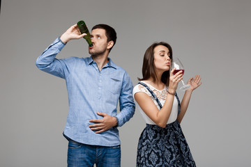 Young beautiful couple drinking wine and beer over grey background.