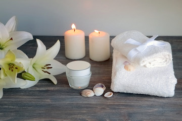 Piece of spa interior with flowers of lily, candles, towels, tissue, napkins, cosmetic product, special light. Copy space. White background.