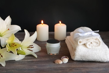 Fototapeta na wymiar Piece of spa interior with flowers of lily, candles, towels, tissue, napkins, cosmetic product, special light. Copy space.Black background.