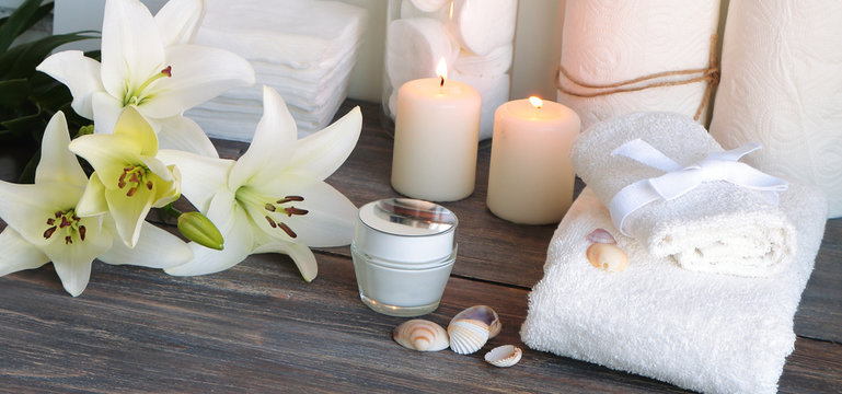 Piece of spa interior with flowers of lily, candles, towels, tissue, napkins, cosmetic product, wide image