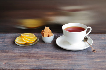 Fototapeta na wymiar Cup of hot steaming black tea on wooden table with brown sugar and lemon. 