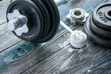 Classic dumbbell with protein powder on rustic wooden table
