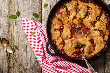 Cherry Cobbler with cinnamon and chocolate on a rough wooden board with cloth and leaves of cherry  - 117437792
