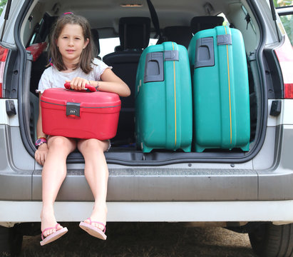 little girl with brown hair long loads the suitcase in the trunk