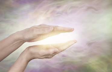 Golden healing aura - female hands held in parallel position with a golden glow between on a subtle  radiating light energy field streaming outwards with copy space