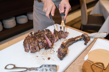 Chef with knife and fork. Professional chef in a restaurant or hotel prepares or cut up t-bone steak.
