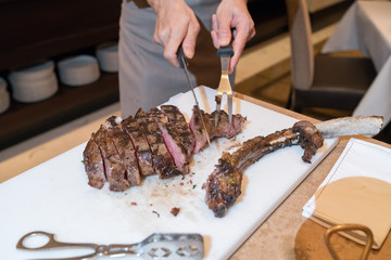 Chef with knife and fork. Professional chef in a restaurant or hotel prepares or cut up t-bone steak.
