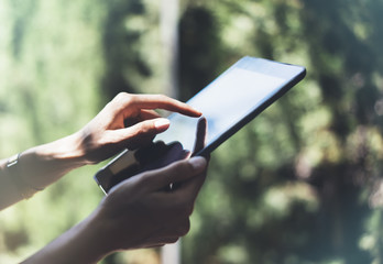 Hipster texting message on tablet or technology mock up. Person using computer on green background. Female hands holding gadget on blurred backdrop mockup. Social networking concept