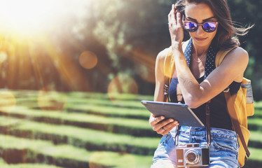 Hipster young girl with backpack using tablet or holding gadget, flare. View tourist traveler with sunglasses on background Barcelona. Mock up for text message. Social networking and vacation concept