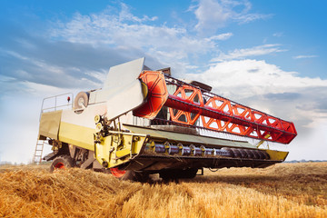 Combine-harvester collecting wheat grain. Close-up. Cloud blue sky. Horizontal. Working concept
