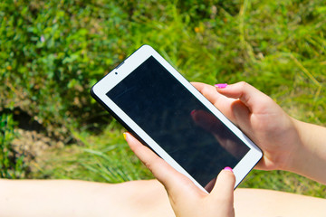 Woman's hands holding a tablet laying on grass