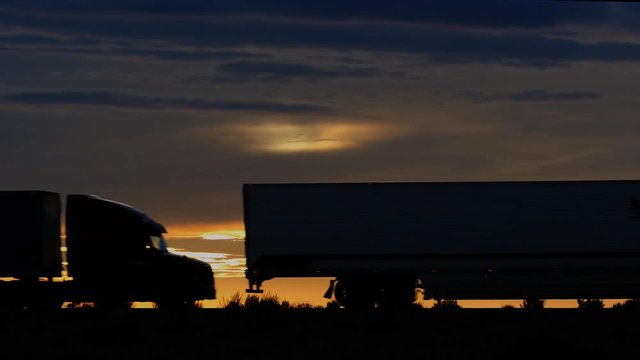 Silhouette of 3 semi trucks passing at sunset