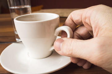 Male hand holds white cup of espresso