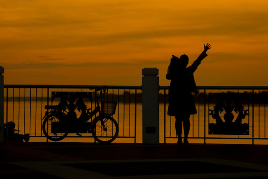 Silhouette of happy young woman with bicycle at sunset.