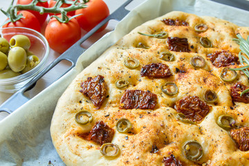 Freshly baked traditional Italian focaccia bread with green olives and sun-dried tomatoes, selective focus