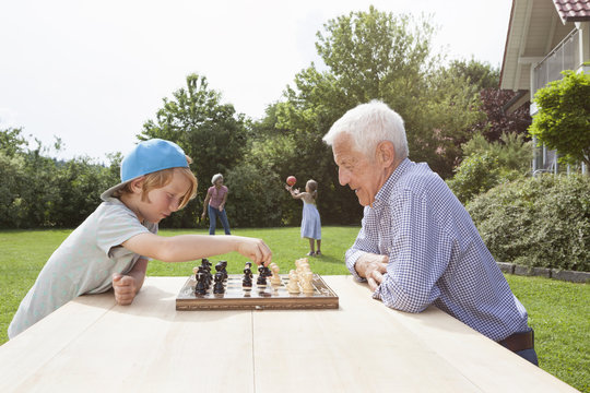Grandfather and grandson playing chess in garden