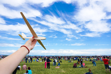 Girl holding toy wood plane at an airshow with crowd in the back - obrazy, fototapety, plakaty