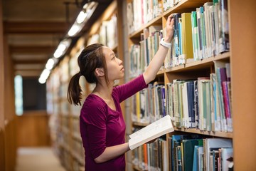 Young woman selecting book in library