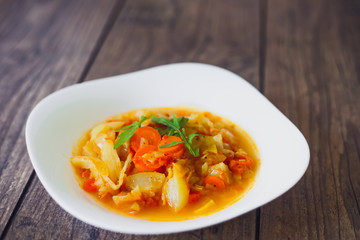 Stewed vegetables in a white bowl on wooden table, selected focus.