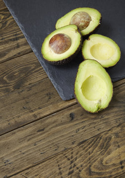 Halved avocados on a slate and distressed wooden kitchen counter background