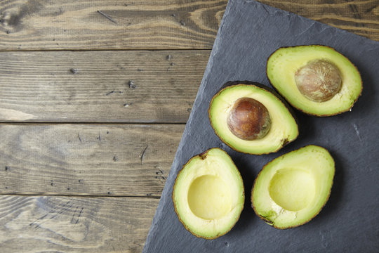 Halved avocados on a distressed wooden counter top and slate background