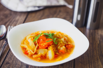 Stewed vegetables in a white bowl on wooden table, selected focus.