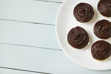 A plate of birthday cupcakes with chocolate frosting on a painted wooden table top background
