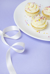 Birthday cup cakes with vanilla frosting and sprinkles on a purple background with a white silk ribbon