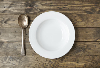An empty white dinner bowl and spoon on a reclaimed wooden background
