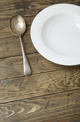 An empty white dinner dish and spoon on a distressed wooden background