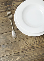 An empty white dinner dish and fork on a distressed wooden background