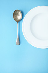 An empty white bowl and spoon on a blue background