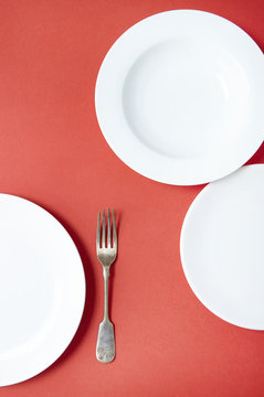 Empty white dinner plates and a fork on a red background
