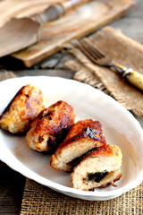 Small stuffed meat rolls on a plate. Fork, cutting board on old wooden table. Roasted Turkey breast rolls with cheese and mushrooms. Festive food recipe. Rustic style. Closeup