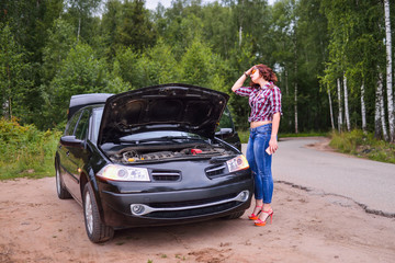 Frustrated young woman looking at broken down car engine