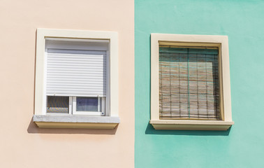 two windows with colorful facade of a residential building wooden shutters orange and green pastel
