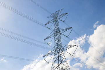 Fototapeta premium Electricity pylon silhouetted against blue sky wih cloud background. High voltage tower