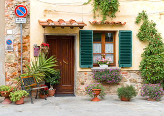 Wooden door and window with flower pots in the medieval tuscan town Lucignano. The words "PASSO CARRABILE" on the roadsign mean "keep entrance clear"