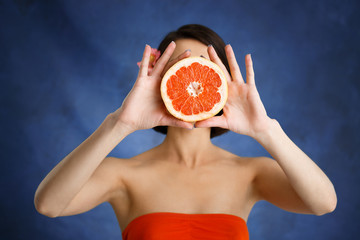 Close up portrait of tender young girl holding cut orange over blue background