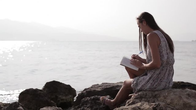 Yong woman making notes in diary on the beach