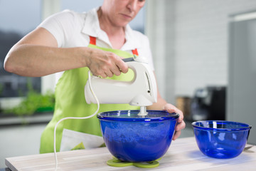 Eine Frau in moderner Küche rührt einen Teig in blauer Schüssel mit dem elektrischen Handrührgerät
