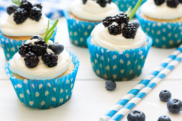 Homemade cupcakes with frosting, blueberries, blackberries and rosemary leaves