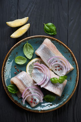Herring fillet with onion, lemon and basil, black wooden surface