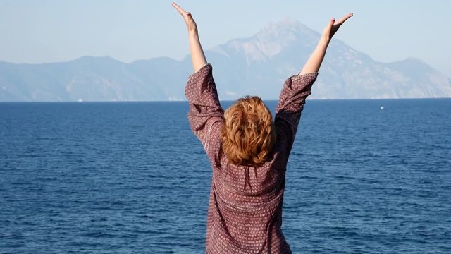 Woman with hands up standing on the top of the hill near the sea