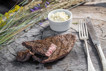 Beef steak on a rustic wooden log, with garlic sauce and old cutlery