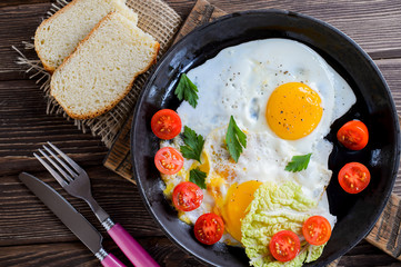 Fried eggs in pan with tomato, bread, pepper and parsley on wooden background