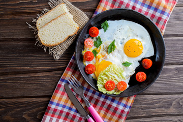 Fried eggs in pan with tomato, bread, pepper and parsley on wooden background